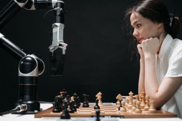 Kobieta gra w szachy z ramieniem robotycznym.