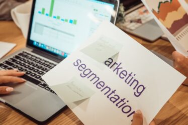 kobieta siedząca przed komputerem i trzymająca w ręce kartę z napisem "marketing segmentation"