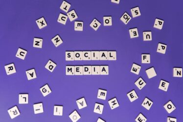 Rozrzucone klocki scrabble z literami układające się w napis SOCIAL MEDIA na fioletowym tle.