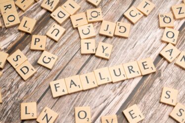 Litery ze gry Scrabble ułożone w słowo „FAILURE” na drewnianym stole.