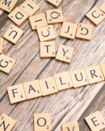 Litery ze gry Scrabble ułożone w słowo „FAILURE” na drewnianym stole.