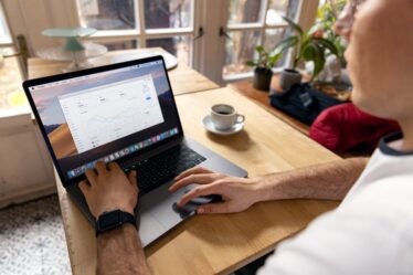 Mężczyzna pracuje na laptopie przy drewnianym stole obok filiżanki kawy.
