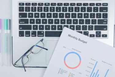 Laptop, okulary, kolorowe długopisy i dokumenty finansowe