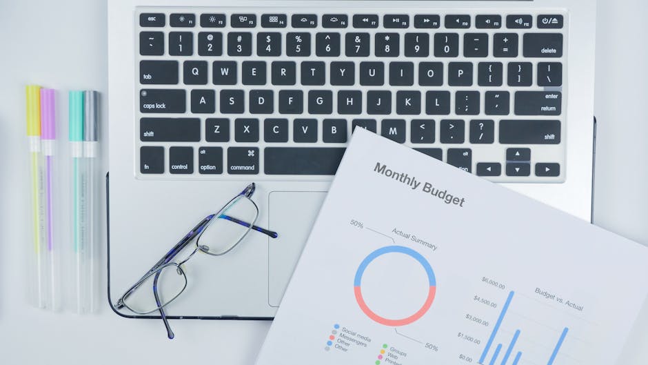 Laptop, okulary, kolorowe długopisy i dokumenty finansowe