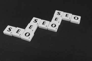 Białe płytki z literami ułożone w schodkowy napis SEO na czarnym tle.