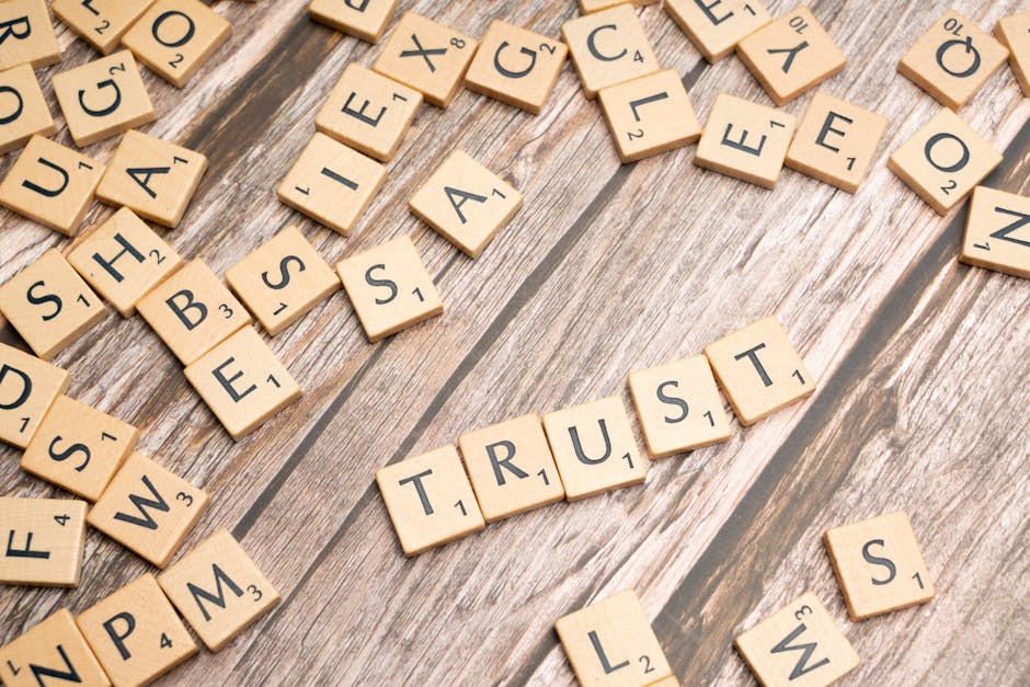 Drewniane klocki z literami ułożone w napis TRUST na drewnianym tle.