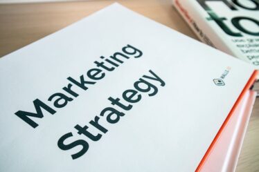 Biała okładka książki z napisem Marketing Strategy leżąca na drewnianym stole.