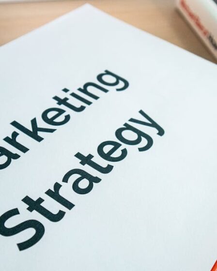 Biała okładka książki z napisem Marketing Strategy leżąca na drewnianym stole.