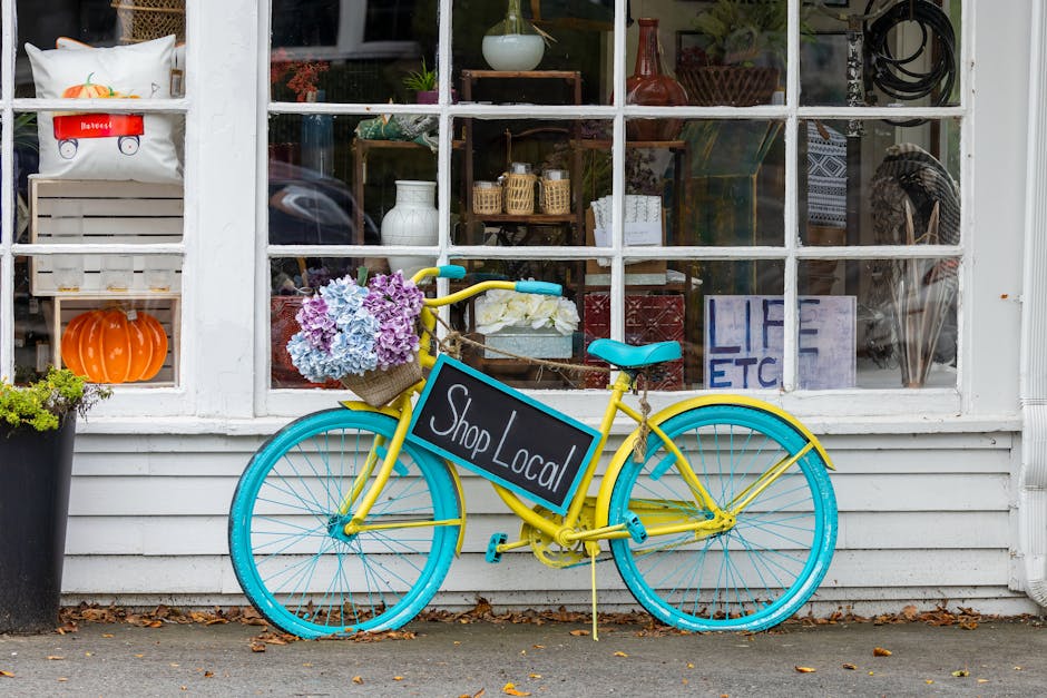 Żółty rower z turkusowymi kołami i tabliczką „Shop Local” przed witryną sklepową.