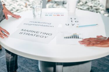 Osoby omawiające dokumenty dotyczące marketingu przy okrągłym białym stole w biurze.