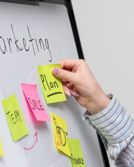 kobieca ręka przyklejająca sticky notes do białej tablicy z napisem "marketing"