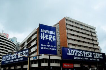 Wielkoformatowe reklamy z napisami „Advertise Here” na elewacji wysokiego biurowca w mieście.