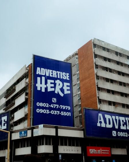Wielkoformatowe reklamy z napisami „Advertise Here” na elewacji wysokiego biurowca w mieście.