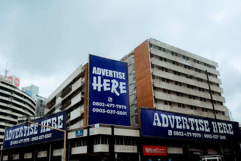 Wielkoformatowe reklamy z napisami „Advertise Here” na elewacji wysokiego biurowca w mieście.