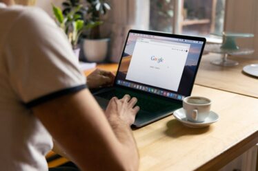 Mężczyzna korzysta z laptopa z otwartą wyszukiwarką Google przy drewnianym stole.