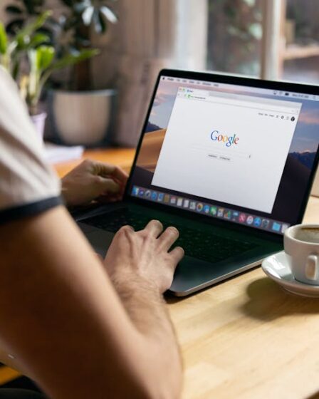 Mężczyzna korzysta z laptopa z otwartą wyszukiwarką Google przy drewnianym stole.