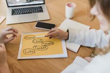 Dwie osoby planują strategię social media, zaznaczając na kartce hasła: friend, chat, share, tweet, like.
