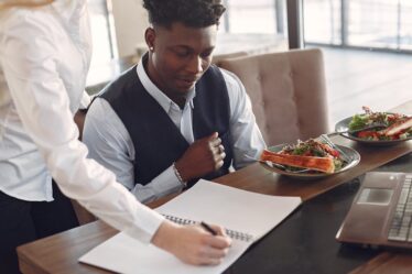 Kobieta i mężczyzna przy stoliku w restauracji pracują z dokumentami i laptopem.