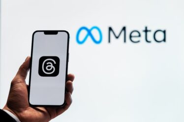 Dłoń trzymająca smartfon z logo aplikacji Threads na tle napisu Meta.