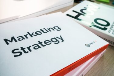Biała teczka z napisem Marketing Strategy leżąca na stosie książek.