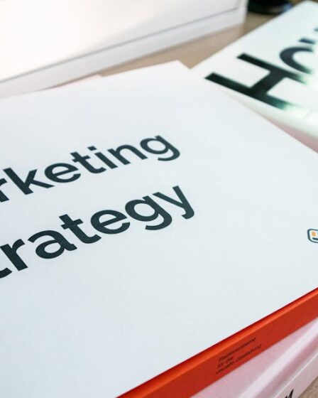Biała teczka z napisem Marketing Strategy leżąca na stosie książek.