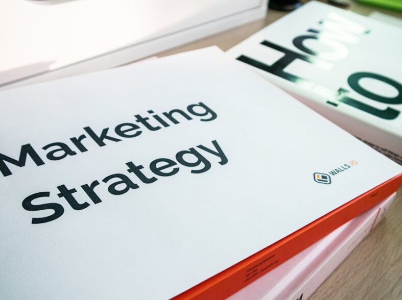 Biała teczka z napisem Marketing Strategy leżąca na stosie książek.