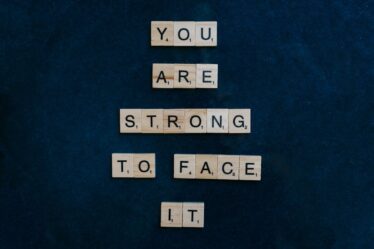 Napis „YOU ARE STRONG TO FACE IT” ułożony z drewnianych klocków do gry Scrabble.