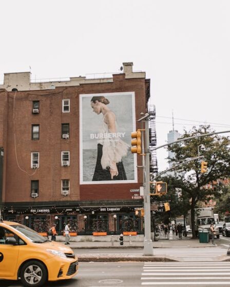 Żółta taksówka na skrzyżowaniu w Nowym Jorku z dużym billboardem Burberry na budynku.