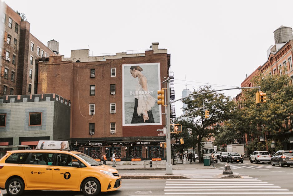 Żółta taksówka na skrzyżowaniu w Nowym Jorku z dużym billboardem Burberry na budynku.