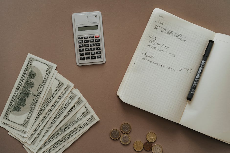 Kalkulator, notatnik z zapiskami finansowymi, banknoty oraz monety na brązowym tle.